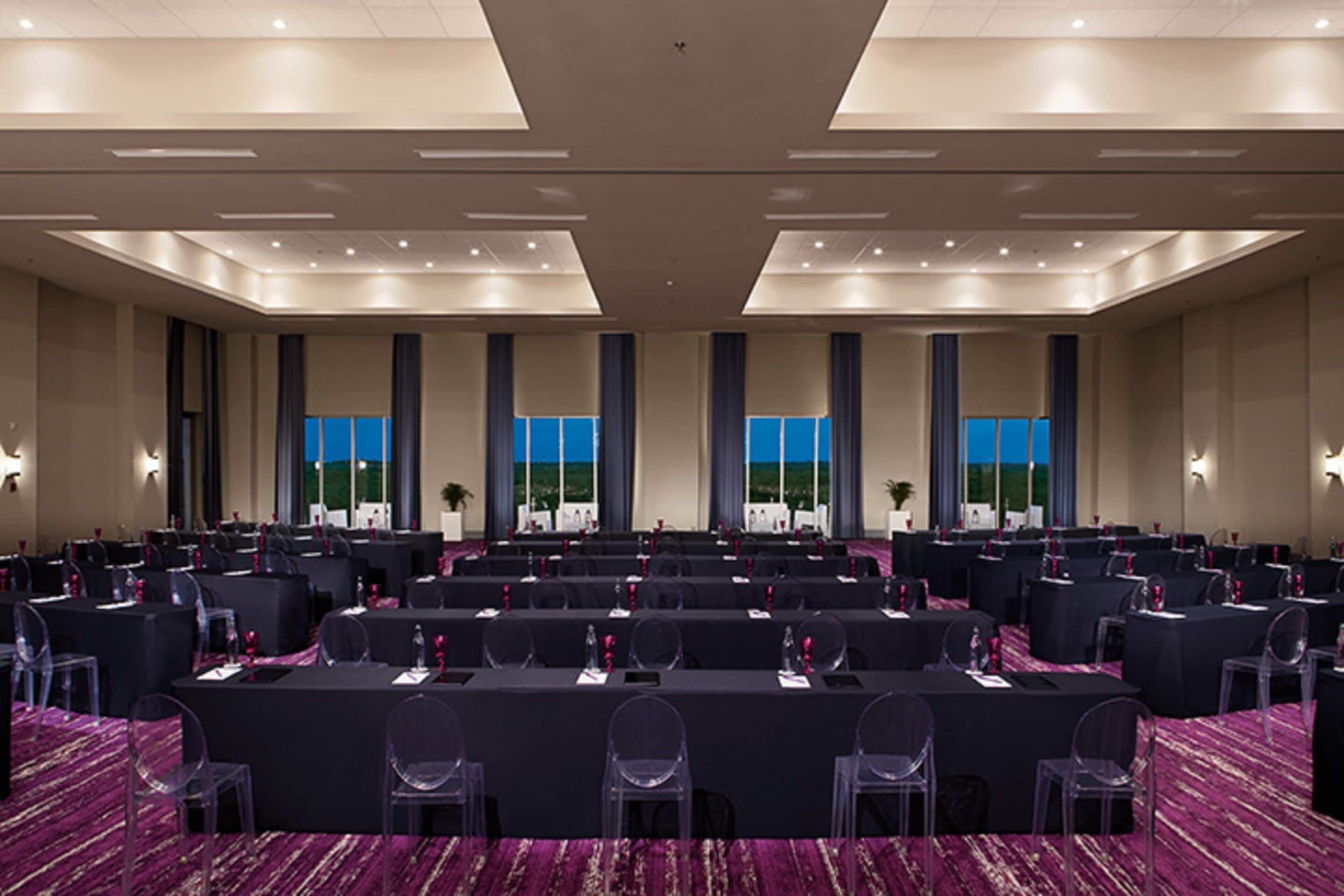 Une salle de conférence dotée de plusieurs tables et chaises, de grandes fenêtres et d’un sol recouvert de moquette.