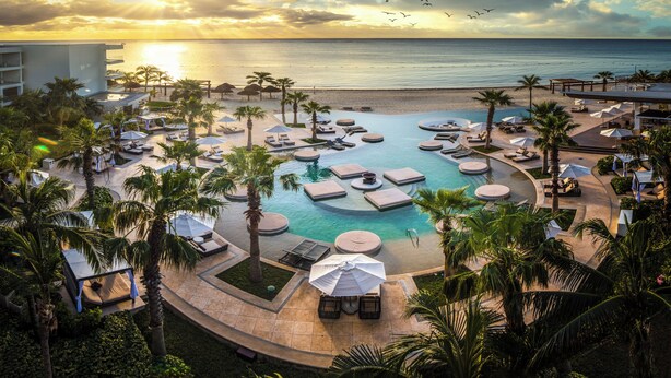 Un resort con piscina, lettini, ombrelloni e palme.