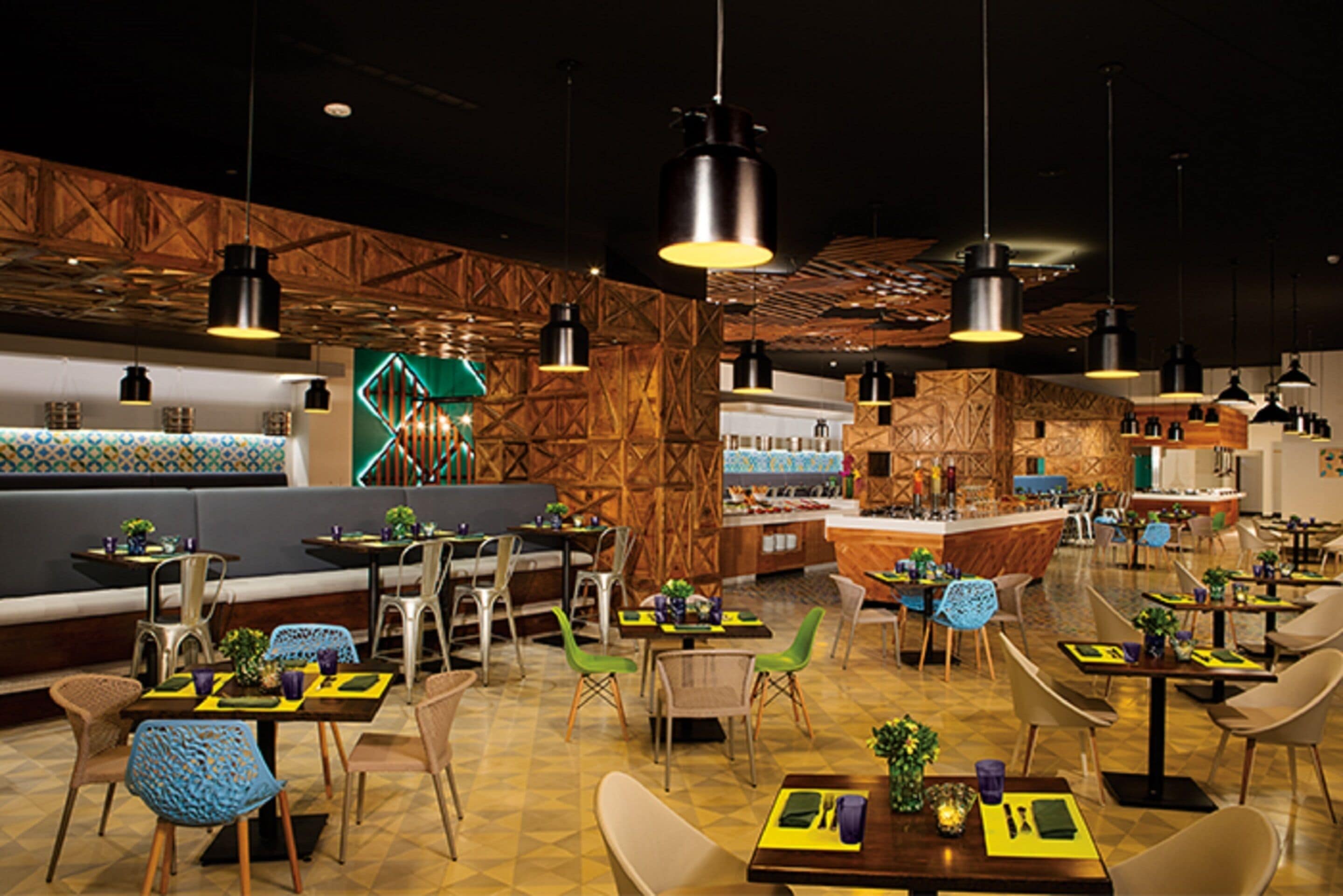 A modern restaurant with high ceilings, exposed wooden beams, and contemporary pendant lighting. Tables are arranged around a central bar area with stools.