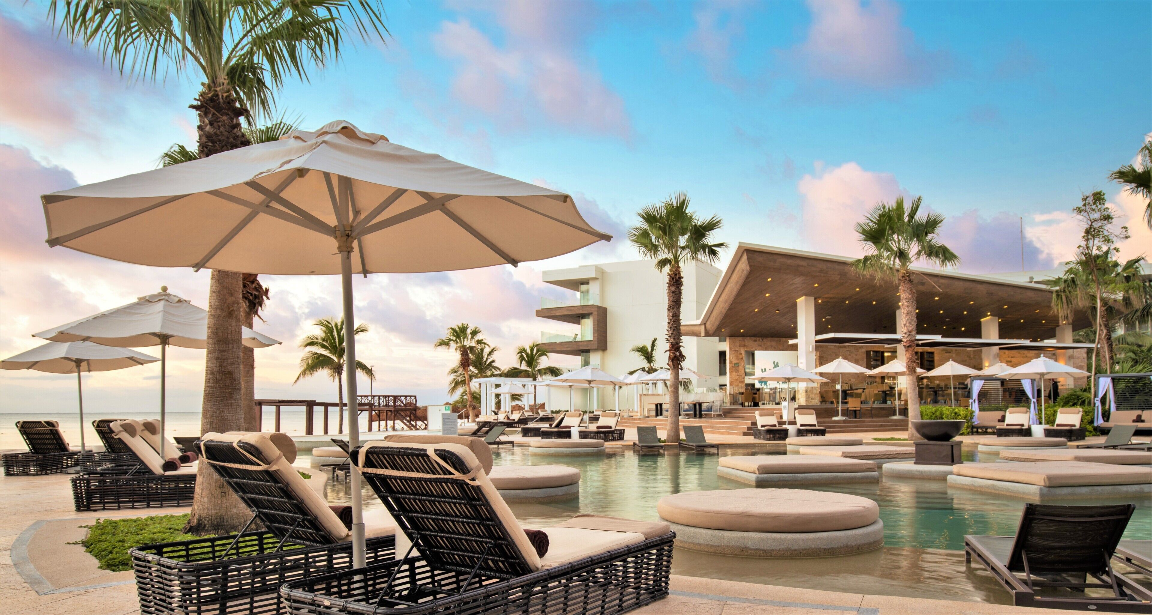 Una piscina al aire libre, sombrillas, sillones reclinables de piscina