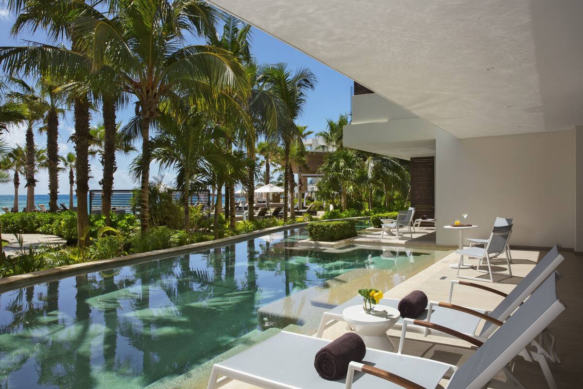 Un espace aménagé au bord de la piscine, avec des chaises longues, une petite table ornée d’un vase de fleurs et une vue sur l’océan.