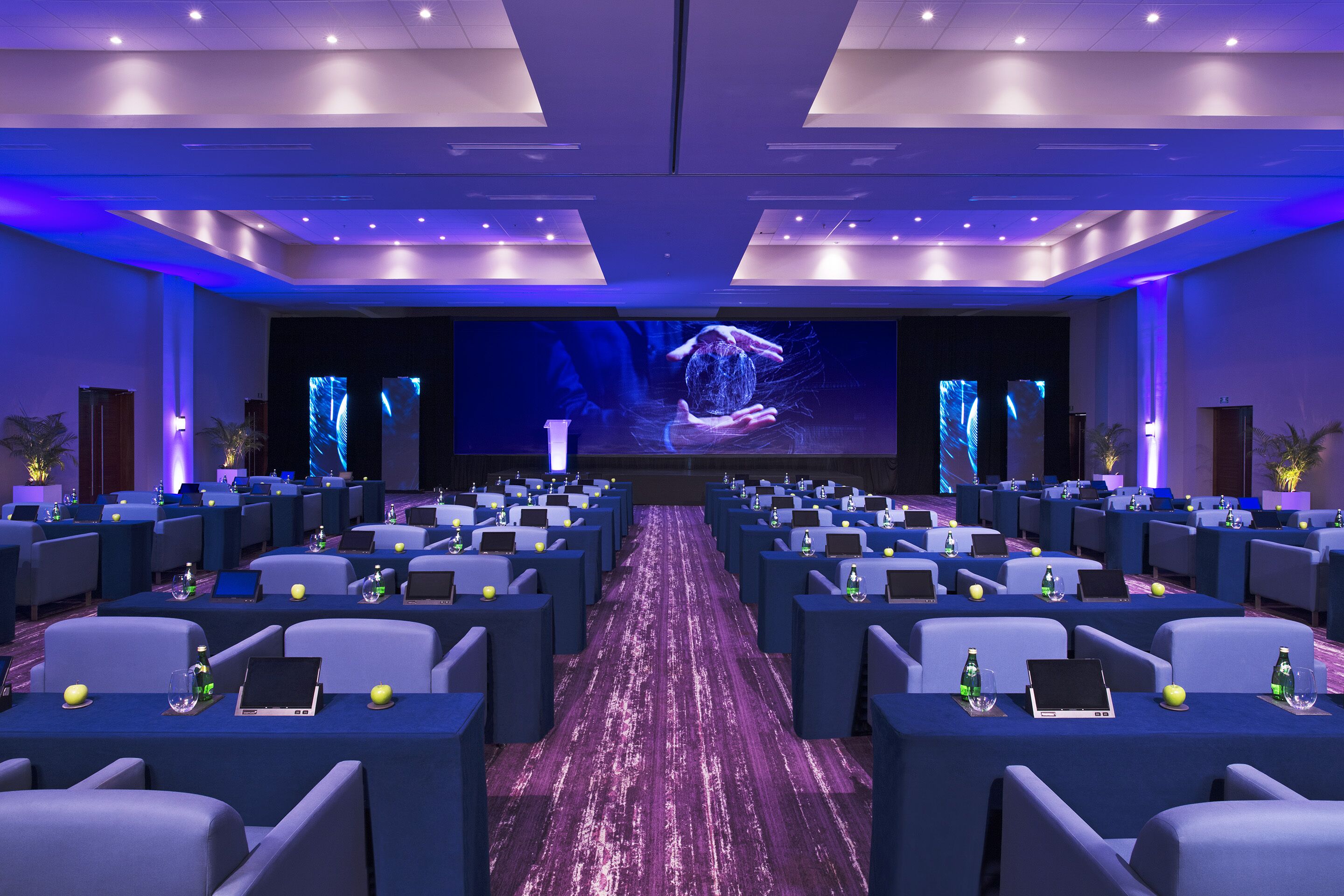 A conference room with rows of tables, chairs, and a large screen at the front.