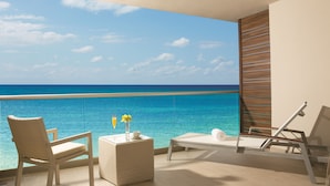 Un balcone con vista sull'oceano, una sedia in vimini, un tavolino con un vaso e un bicchiere, e una poltrona relax.