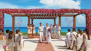 Una cerimonia nuziale in spiaggia, con un arco in legno e decorazioni floreali.