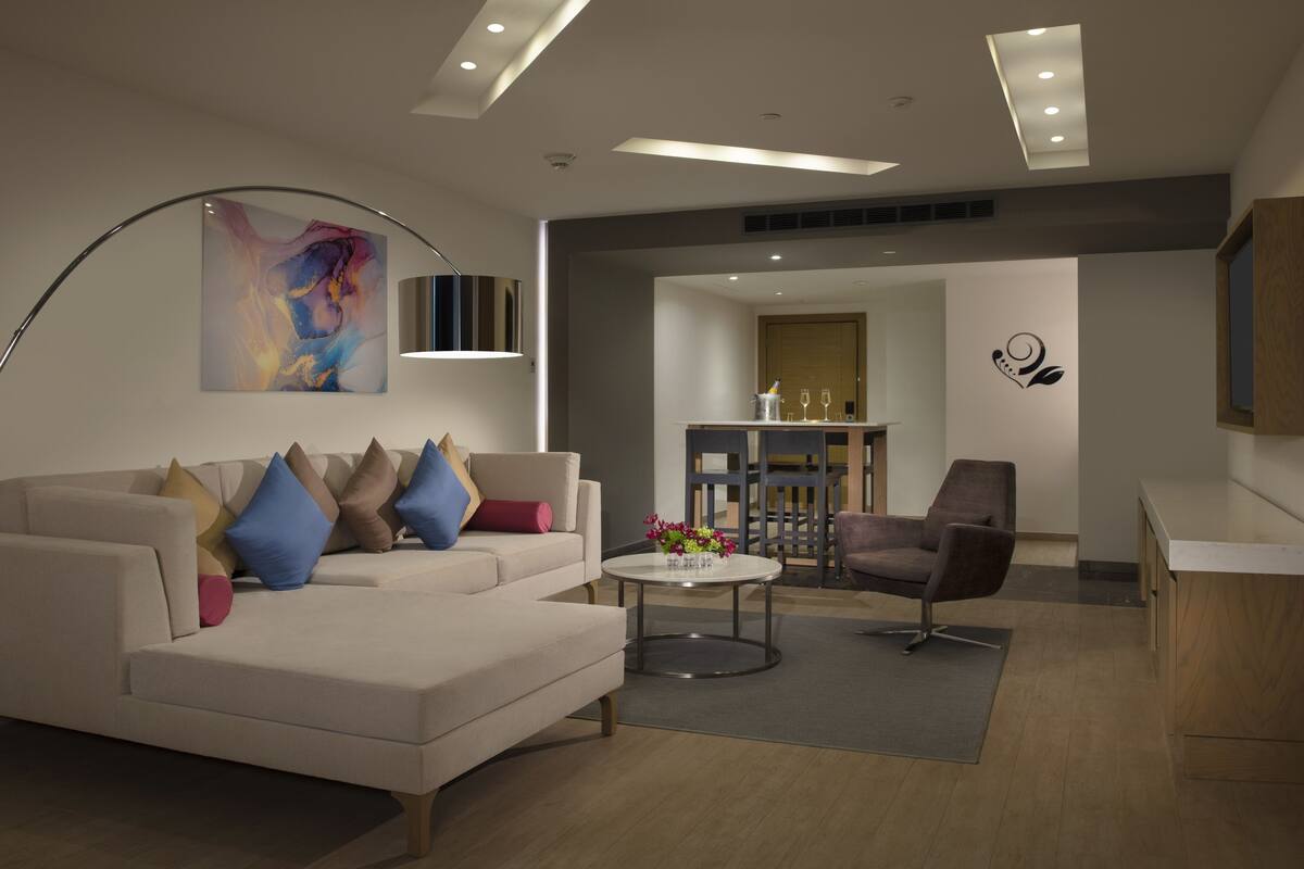 Un salon moderne avec un canapé, un fauteuil et une table basse. Un tableau orne le mur, et on y trouve également une armoire en bois.