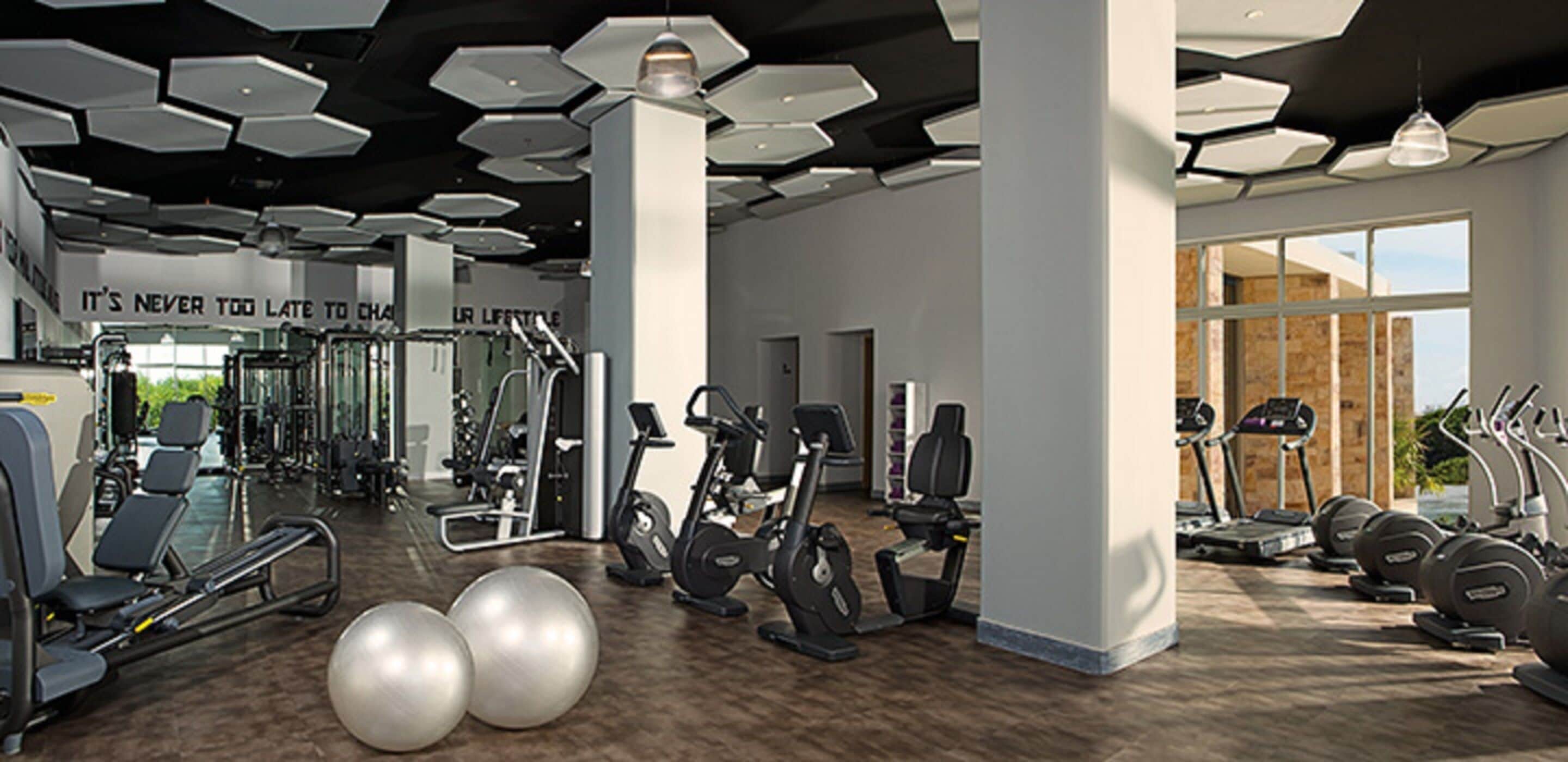 A modern gym with various exercise equipment, large windows, and a motivational quote on the wall.