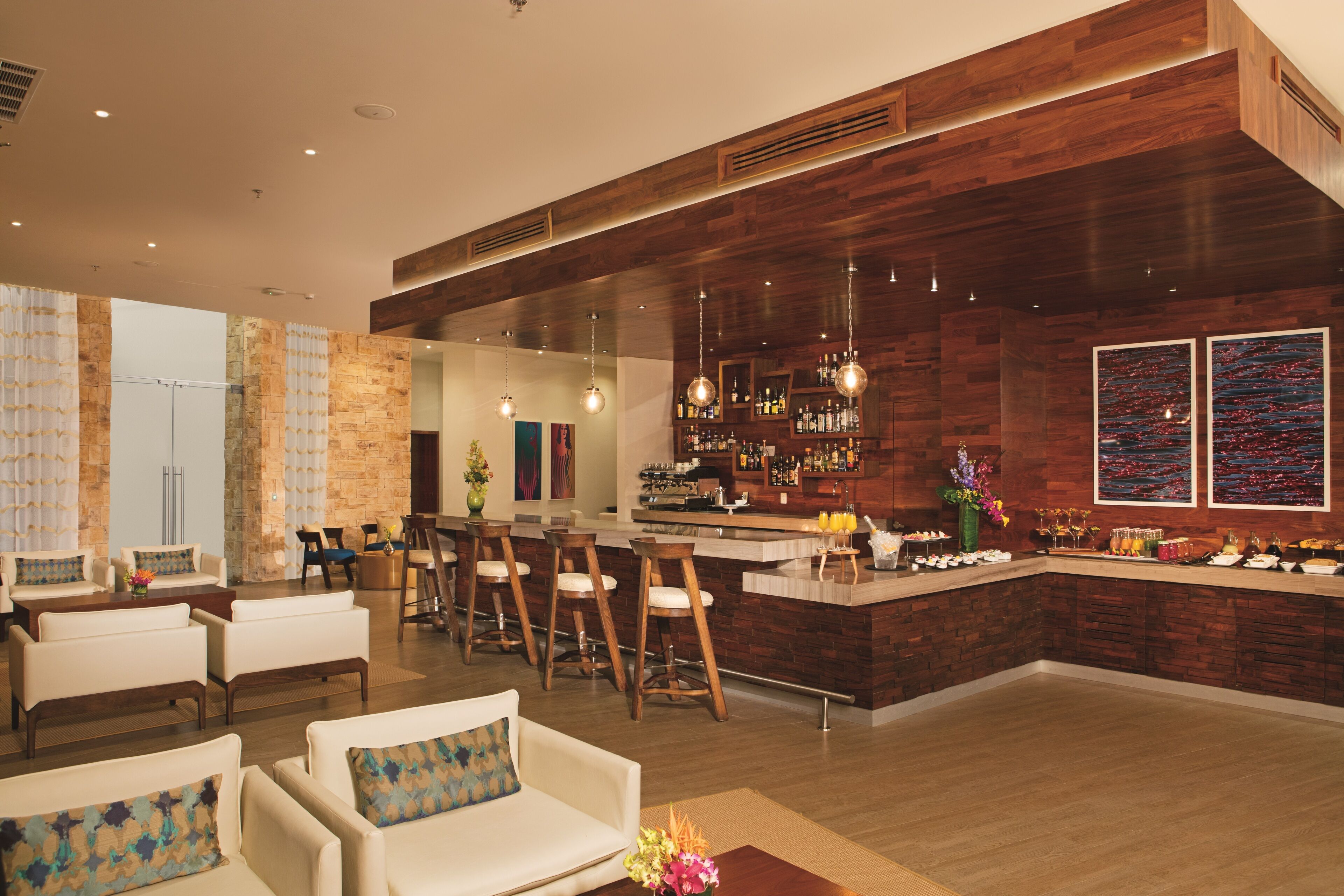 Una zona de bar moderna con mostrador de madera, asientos con taburetes y un espejo grande.