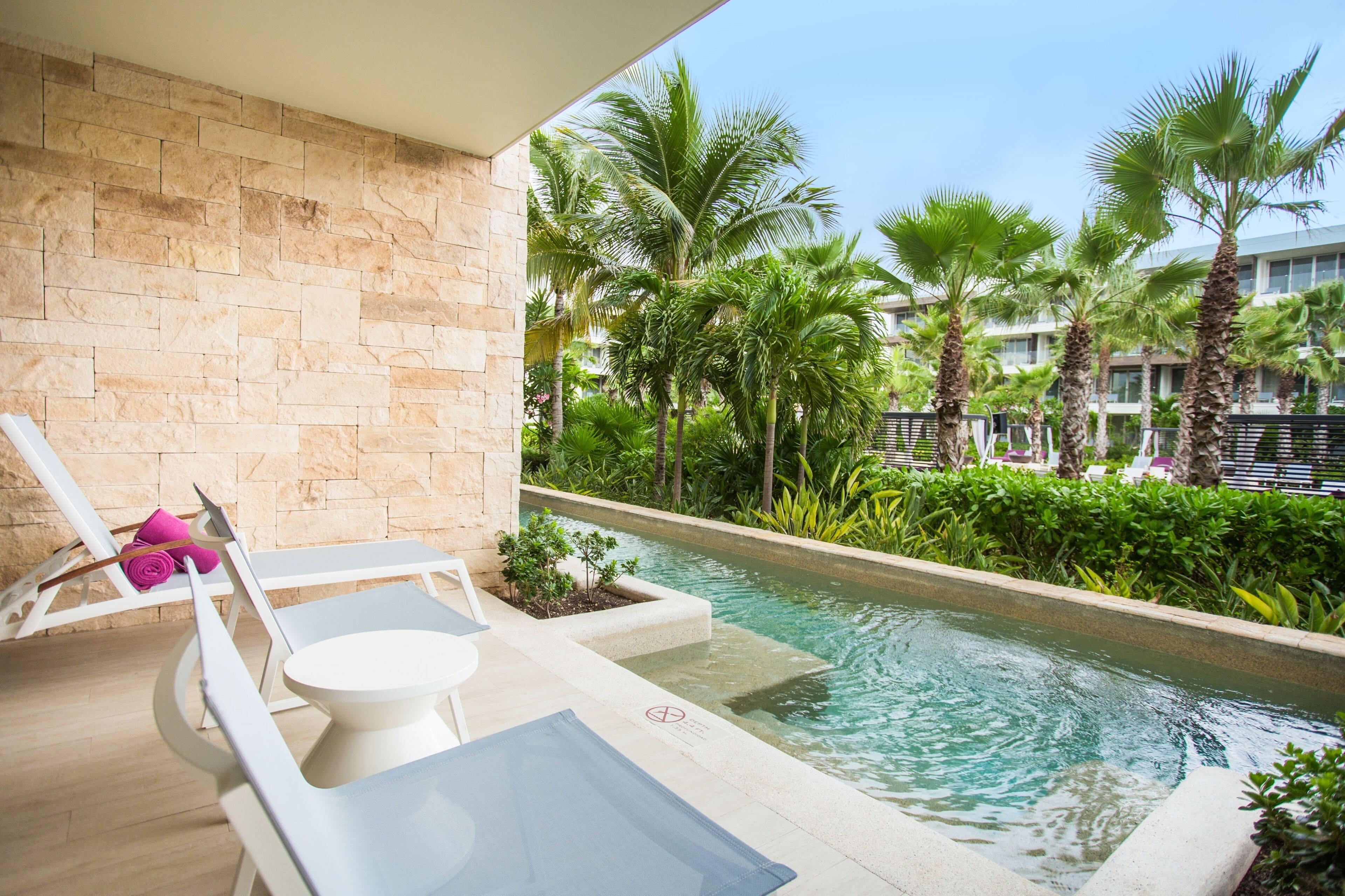 A poolside area with lounge chairs, a small table, and a stone wall.