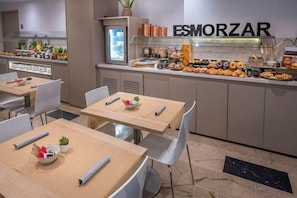 A modern dining area with tables, chairs, and a buffet counter with various food items. - Hotel Serhs Del Port (Barcelona)