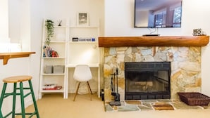 Una sala de estar con chimenea de piedra, un televisor montado y una estantería con libros y objetos decorativos.