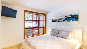 Un dormitorio con cama, ventana con vistas, un cuadro en la pared y televisor montado en la pared.