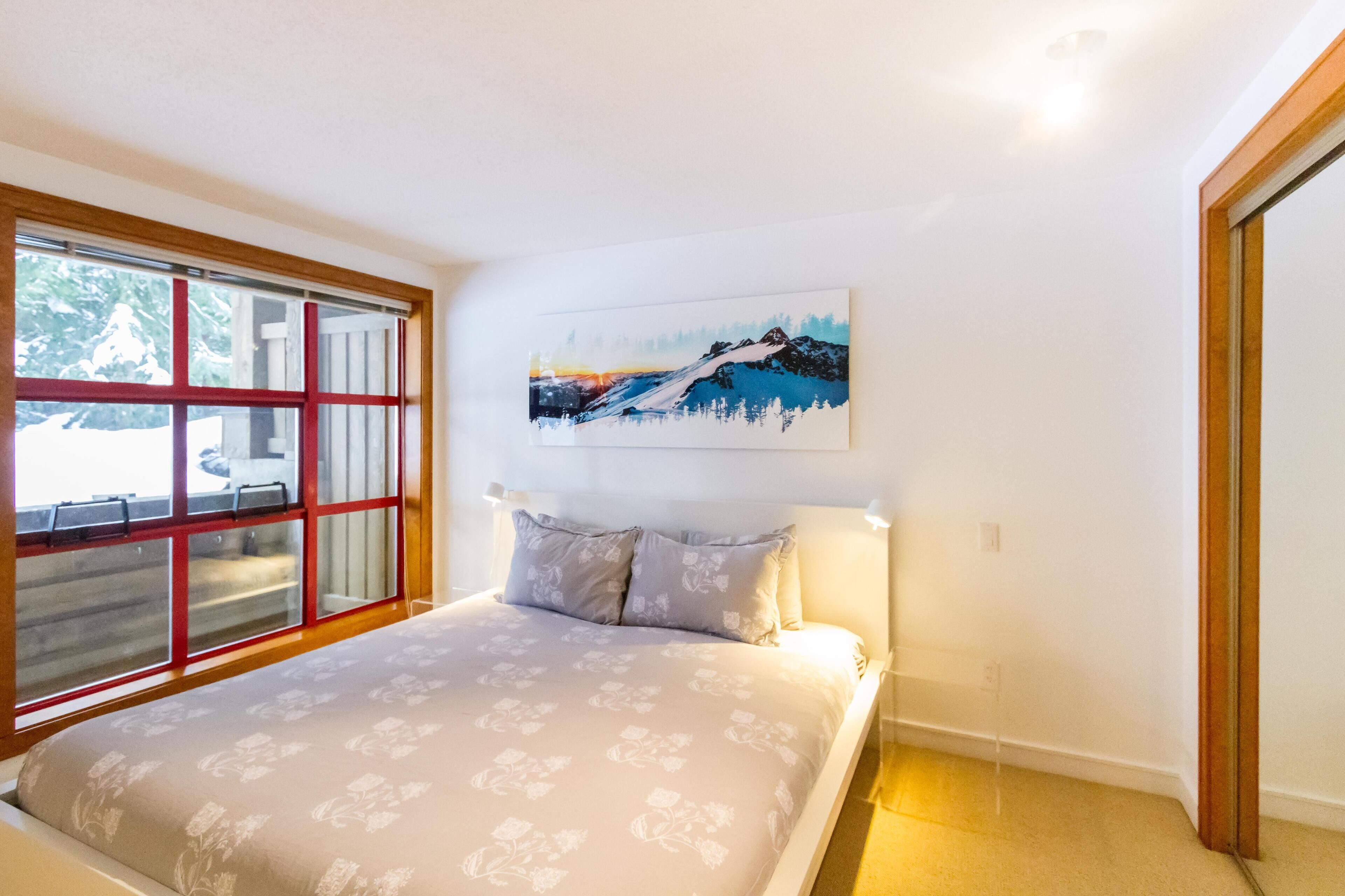 A bedroom with a bed, a window with a view, and a painting on the wall.