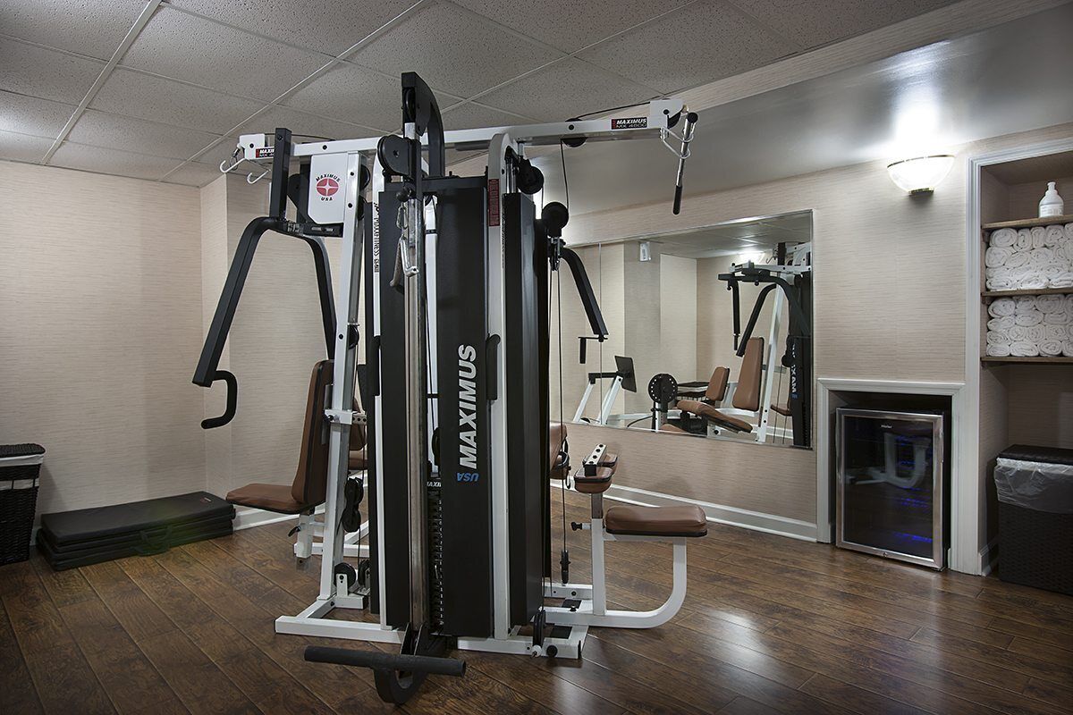 Une salle de sport équipée d'un appareil MAXIMUS, dotée d'un murmiroir et d'un plancher en bois.