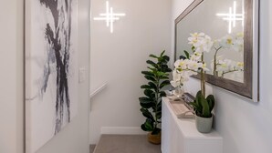 A hallway with a modern abstract painting, a potted plant, and a mirror reflecting white orchids. - Panoramic Views From This Gorgeous 2 Bed Property - Village Location (Whistler)