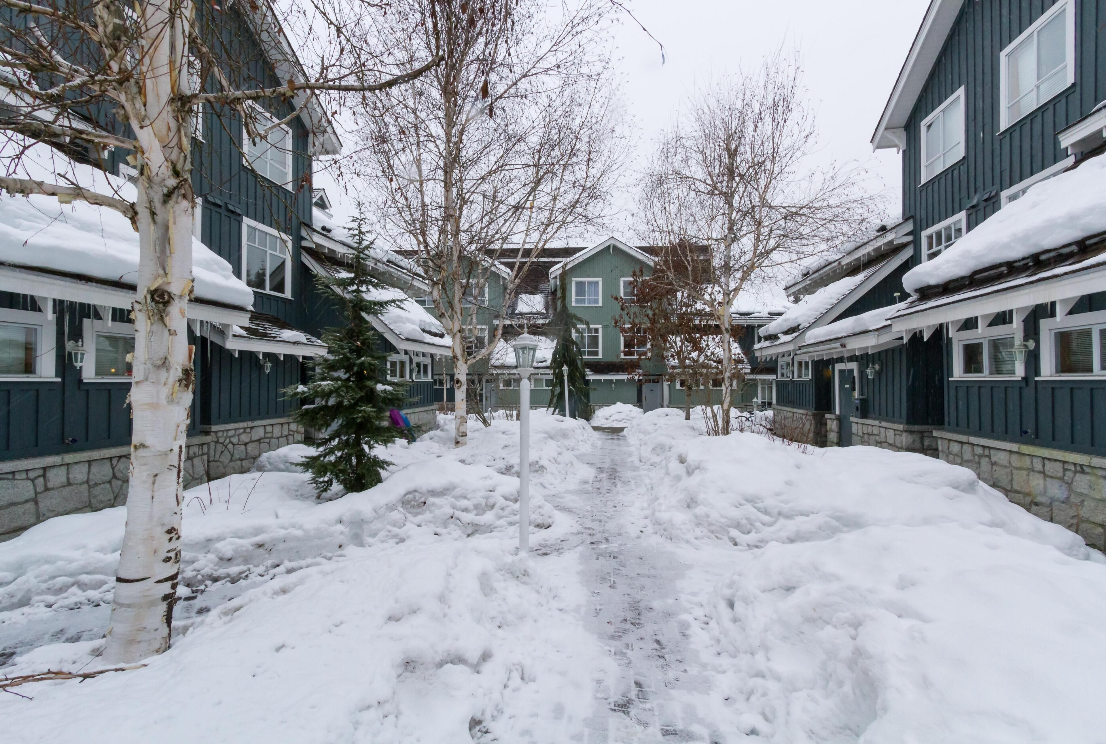A snow-covered pathway leading to a row of two-story buildings with a stone foundation.