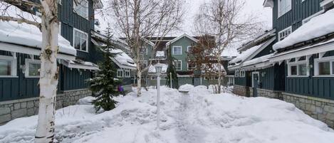 A snow-covered pathway leading to a row of two-story buildings with a stone foundation.