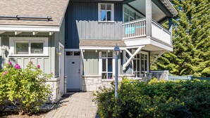 A two-story house with a balcony, stone foundation, and a pathway leading to the entrance. - Panoramic Views From This Gorgeous 2 Bed Property - Village Location (Whistler)