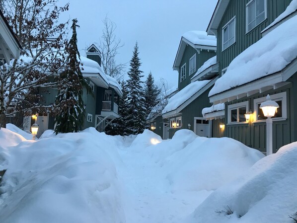 En snedækket gade med bygninger langs begge sider, inklusive balkoner og vinduer med lys.