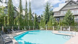 A swimming pool with lounge chairs, surrounded by tall trees and a building with a sloped roof. - Bright and Clean, Walk Everywhere, Shared Pool and Hot Tub (Whistler)
