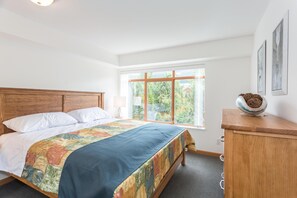 A bedroom with a wooden bed, a large window with a view of greenery, and a wooden dresser. - Bright and Clean, Walk Everywhere, Shared Pool and Hot Tub (Whistler)
