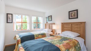 A bedroom with two beds, a wooden headboard, a nightstand with a lamp, and a window with a view of greenery. - Bright and Clean, Walk Everywhere, Shared Pool and Hot Tub (Whistler)