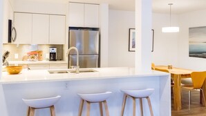 Et moderne køkken med en central ø, rustfrie stålapparater og et spiseområde med træmøbler.