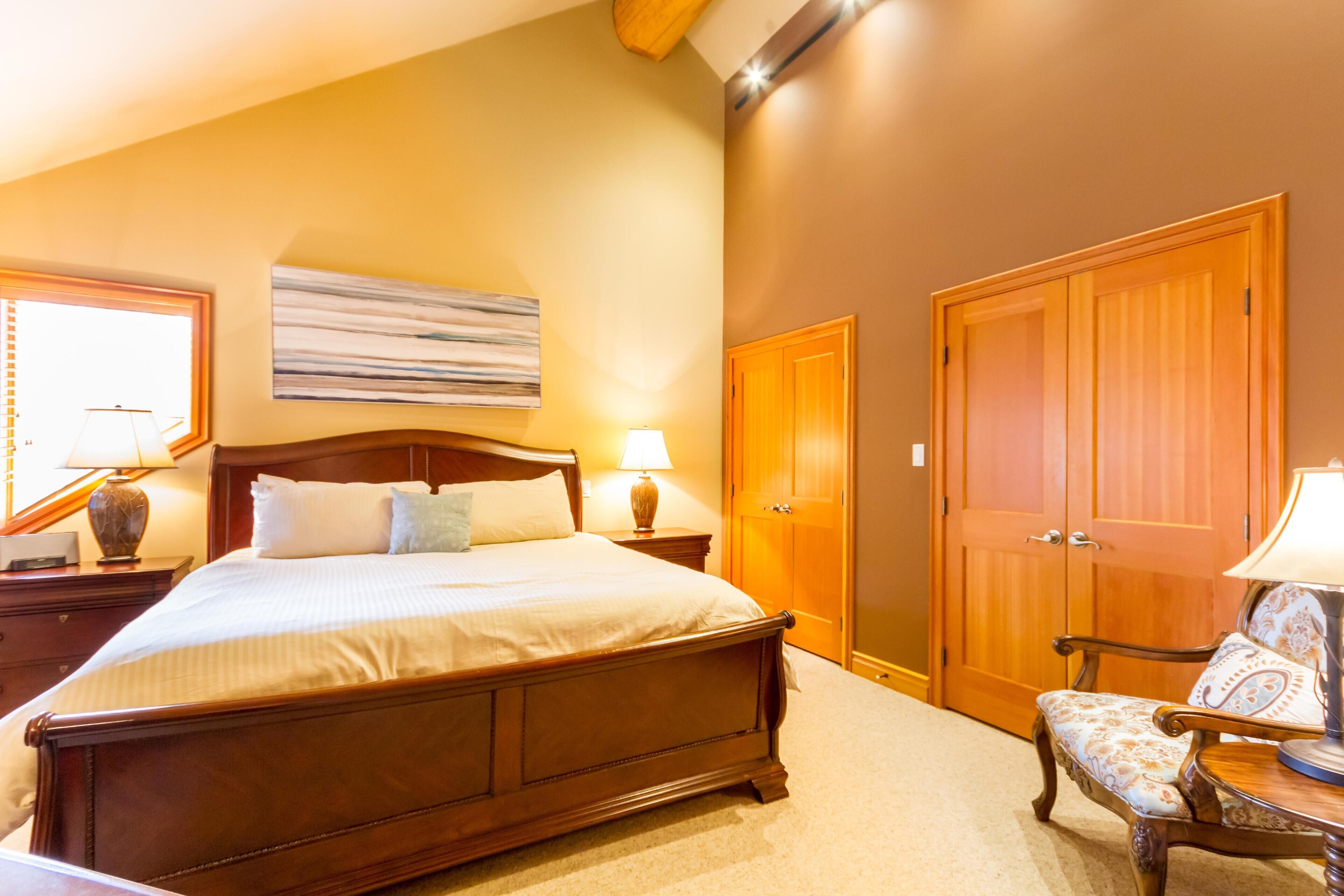 Un dormitorio con una cama grande, un armario de madera y una silla con lámpara.