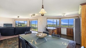 A spacious living area with a glass table, black leather sofa, and a view of the ocean. - With South Beach views, a relaxed family home (PORT FAIRY)