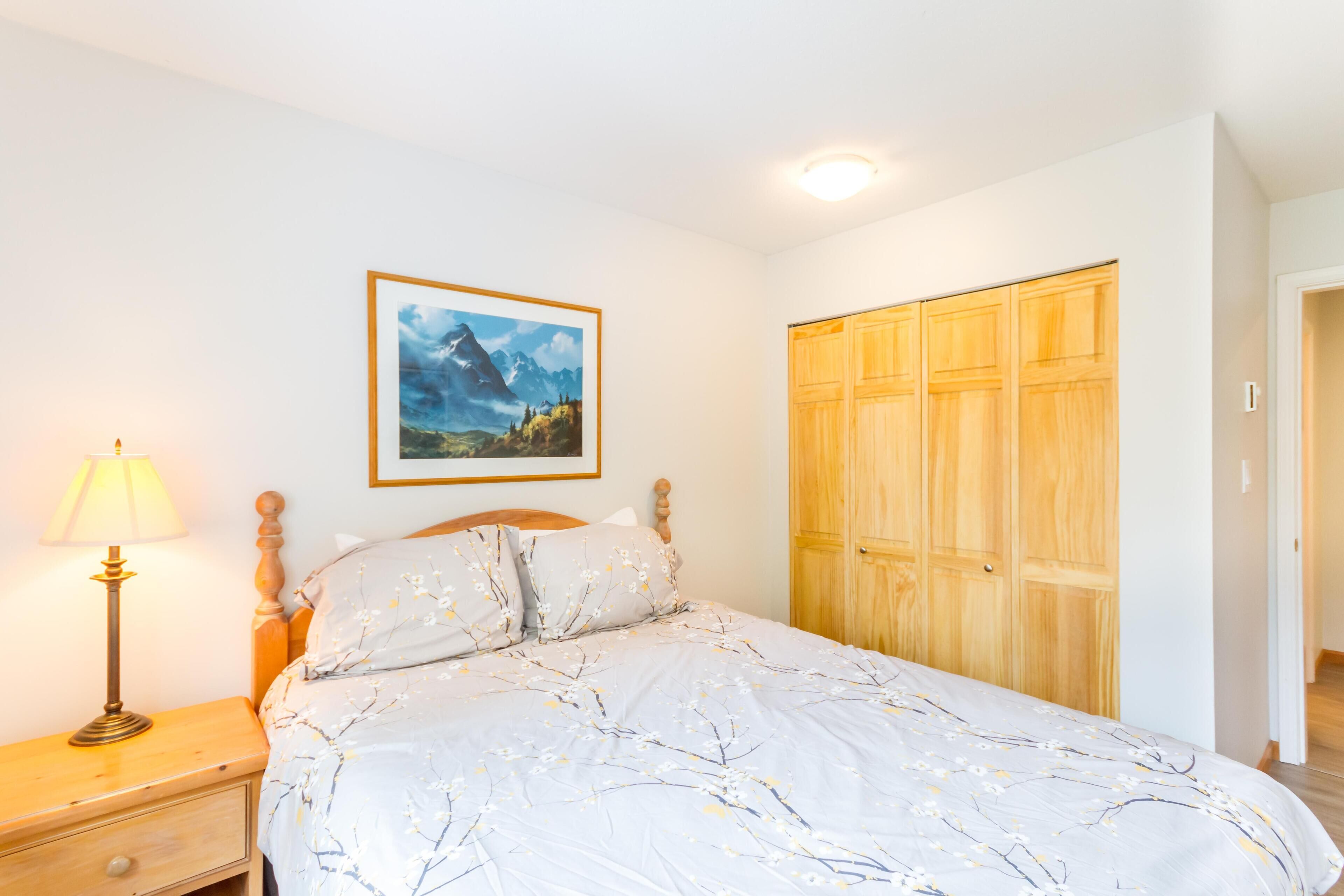 A bedroom with a bed, a nightstand, a lamp, a wardrobe, and a framed picture on the wall.