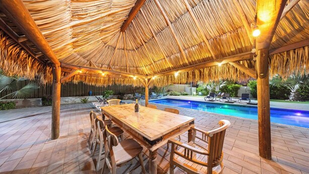 Une terrasse extérieure dotée d’un toit de chaume, d’une piscine et de mobilier en bois.