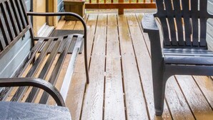 A wooden deck with a railing, two chairs, and a bench.
