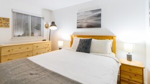 A neatly arranged bedroom with a bed, bedside tables, a dresser, and a window with blinds.
