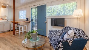 A cozy living room with a zebra-patterned sofa, a glass coffee table with a plant, a kitchen area with white cabinets, and a blue door.