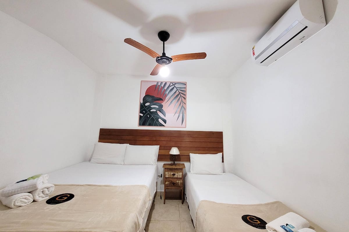 Ein Hotelzimmer mit zwei Einzelbetten, einem Deckenventilator, einer Klimaanlage und einem tropisch gestalteten Wandbild.