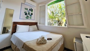 Una habitación de hotel con una cama, un ventilador de techo, una ventana con vistas a árboles y un aire acondicionado de pared.