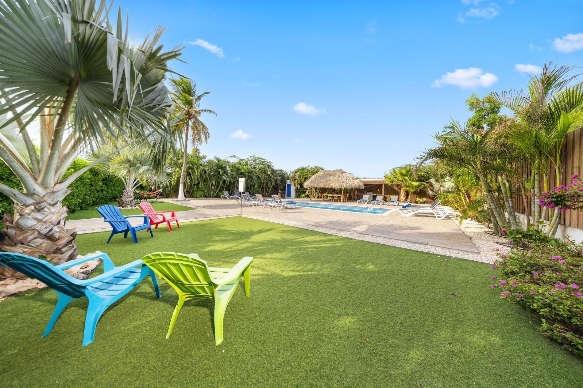 A backyard with a swimming pool, green artificial grass, and colorful lounge chairs.