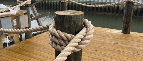 A wooden dock with a rope tied around a post, wooden planks, and a view of houses in the background.