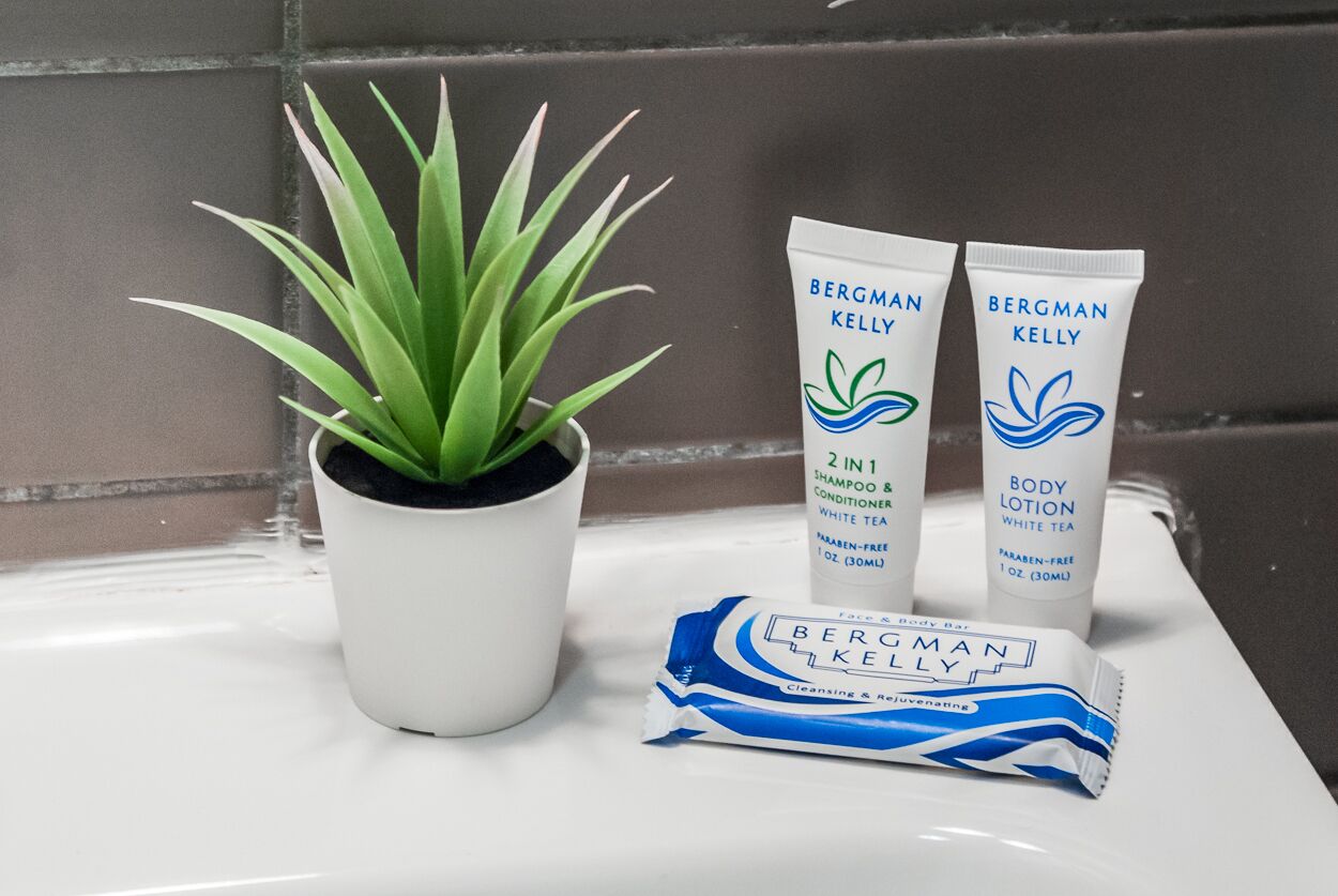 A bathroom sink with two Bergman Kelly body lotion tubes, a face and body bar, and a potted plant.