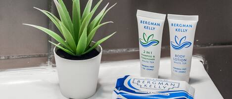 A bathroom sink with two Bergman Kelly body lotion tubes, a face and body bar, and a potted plant.