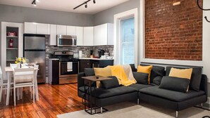 A modern kitchen with stainless steel appliances, a dining area with a white table and chairs, and a black sofa with yellow cushions. - Gorgeous Wooster Sq. apt. - wshr/dryr, parking (New Haven)