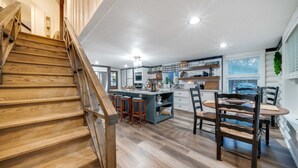 Een moderne keuken met een centraal eiland, een houten trap en een eethoek met stoelen en een tafel.