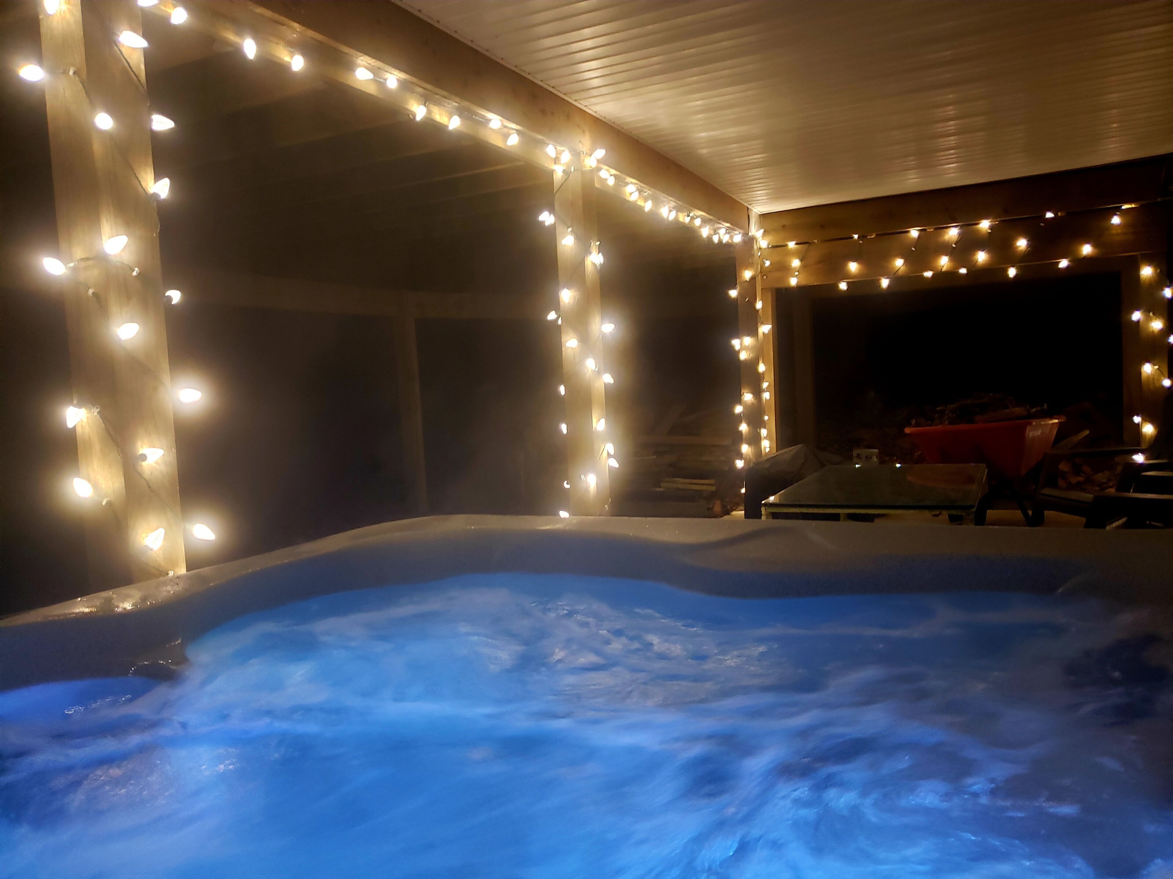 A hot tub surrounded by string lights, wooden walls, and a covered outdoor area.