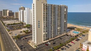 Ein Hochhaus-Hotel mit mehreren Etagen, einem Parkplatz und Blick auf den Strand.