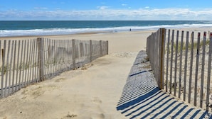 Ein Sandweg am Strand mit Holzzäunen, der zum Meer führt.
