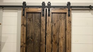 A wooden sliding barn door with metal hardware, set against a white wall. - Circle C Cabin Perfect for Cozy Relaxing Retreats (Caldwell)