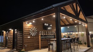 An outdoor bar area with a wooden structure, a sign reading "COLD BEER", and several chairs and tables. - Circle C Cabin Perfect for Cozy Relaxing Retreats (Caldwell)