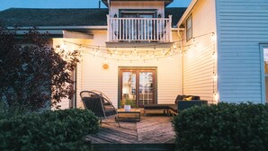 Una casa con balcón, un porche con mobiliario exterior y luces colgantes.
