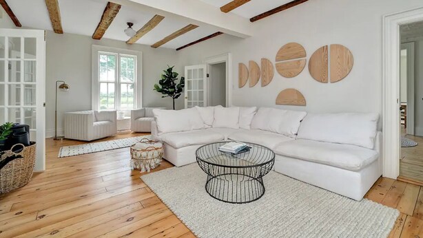 Una sala de estar moderna con un sofá seccional blanco, una mesa de centro de vidrio y vigas de madera en el techo.