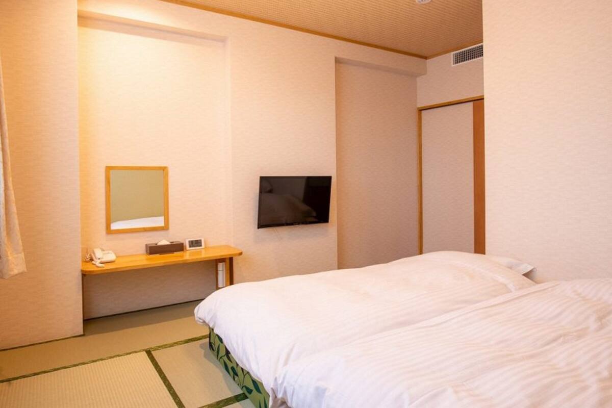 Una camera d'albergo con un letto, un comodino con un telefono, uno specchio e una TV a muro.