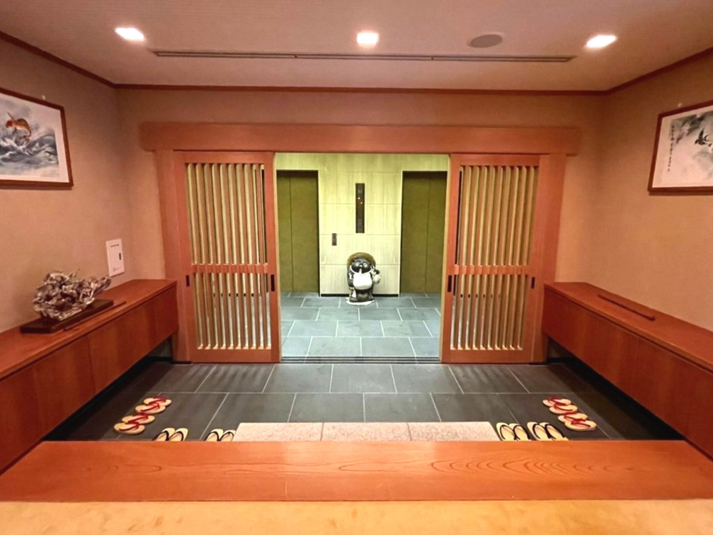A hotel lobby with a traditional Japanese entrance, a reception desk, and a small statue on the left.
